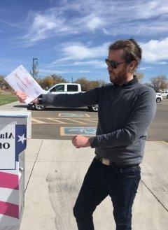 Man with facial hair and sunglasses, standing in parking lot.